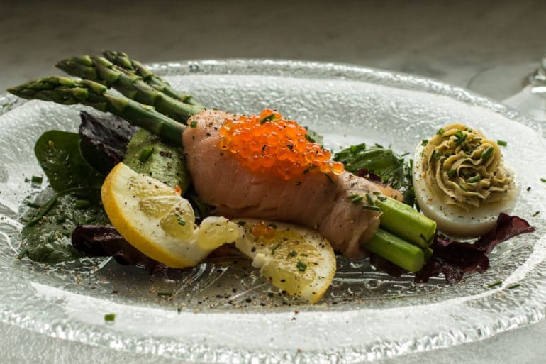 Plated asparagus wrapped in cold smoked salmon with a smoked salmon deviled egg.
