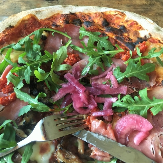 Homemade pizza topped with ham, arugala and pickled onions.